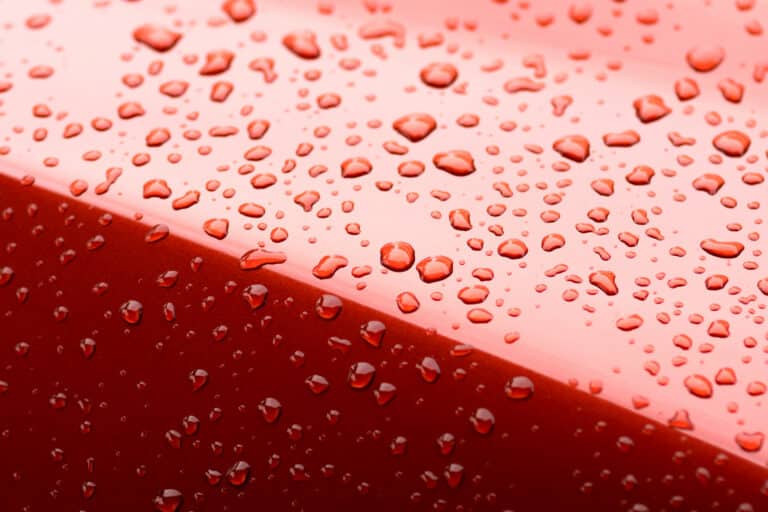 Close-up of red glossy surface with water droplets, showing detail of wet texture and fresh, clean appearance.